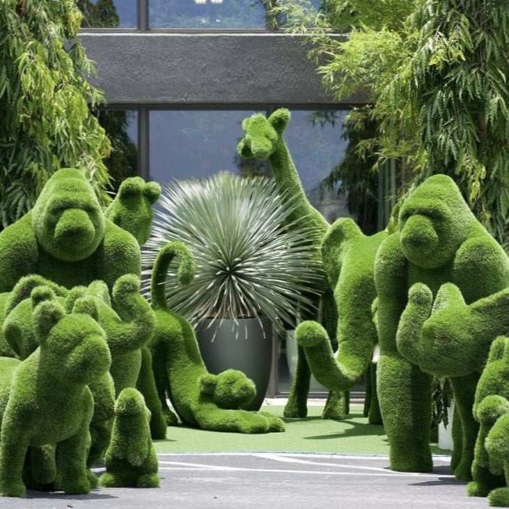 Topiary animals in a manicured garden landscape, including a lion, giraffe, and deer